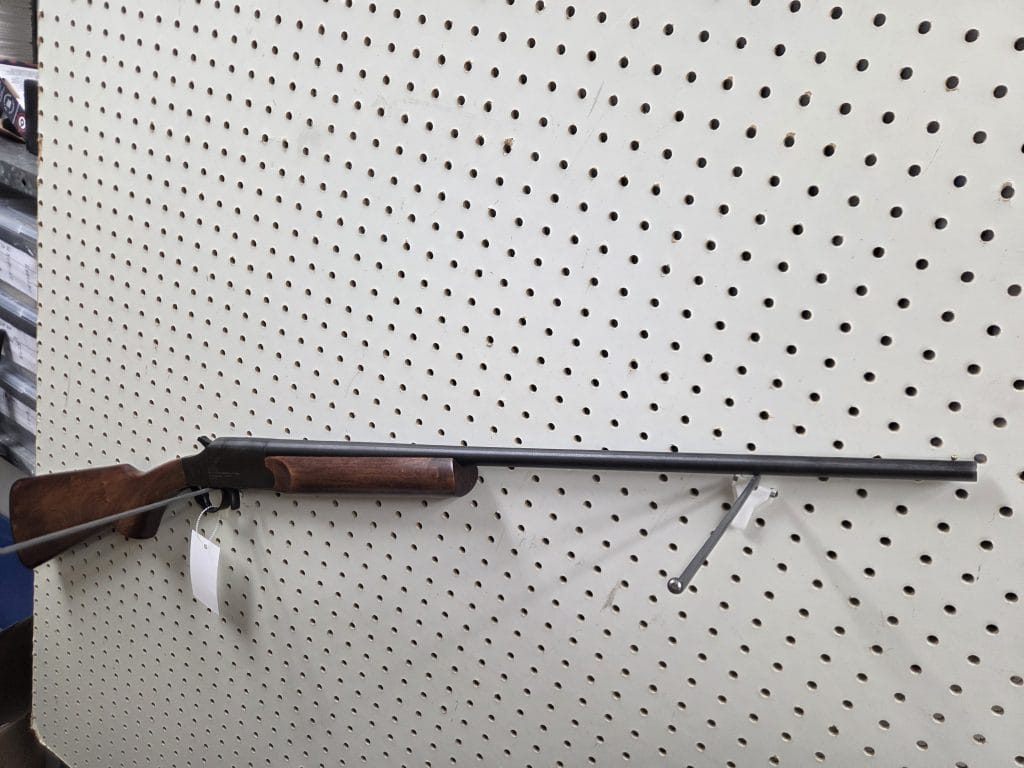 1000014576 single-shot break-action shotgun with a wooden stock on a pegboard display.