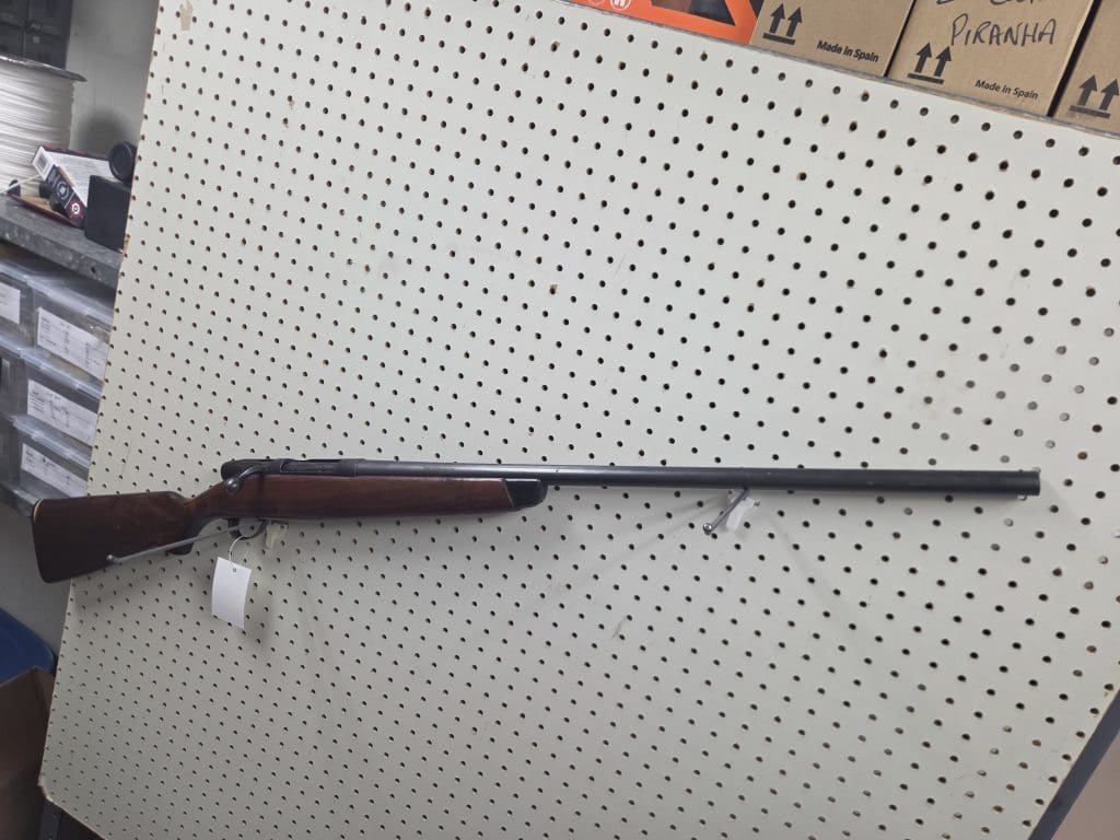 20261018_092021 bolt-action rifle with a wooden stock mounted on a pegboard wall.