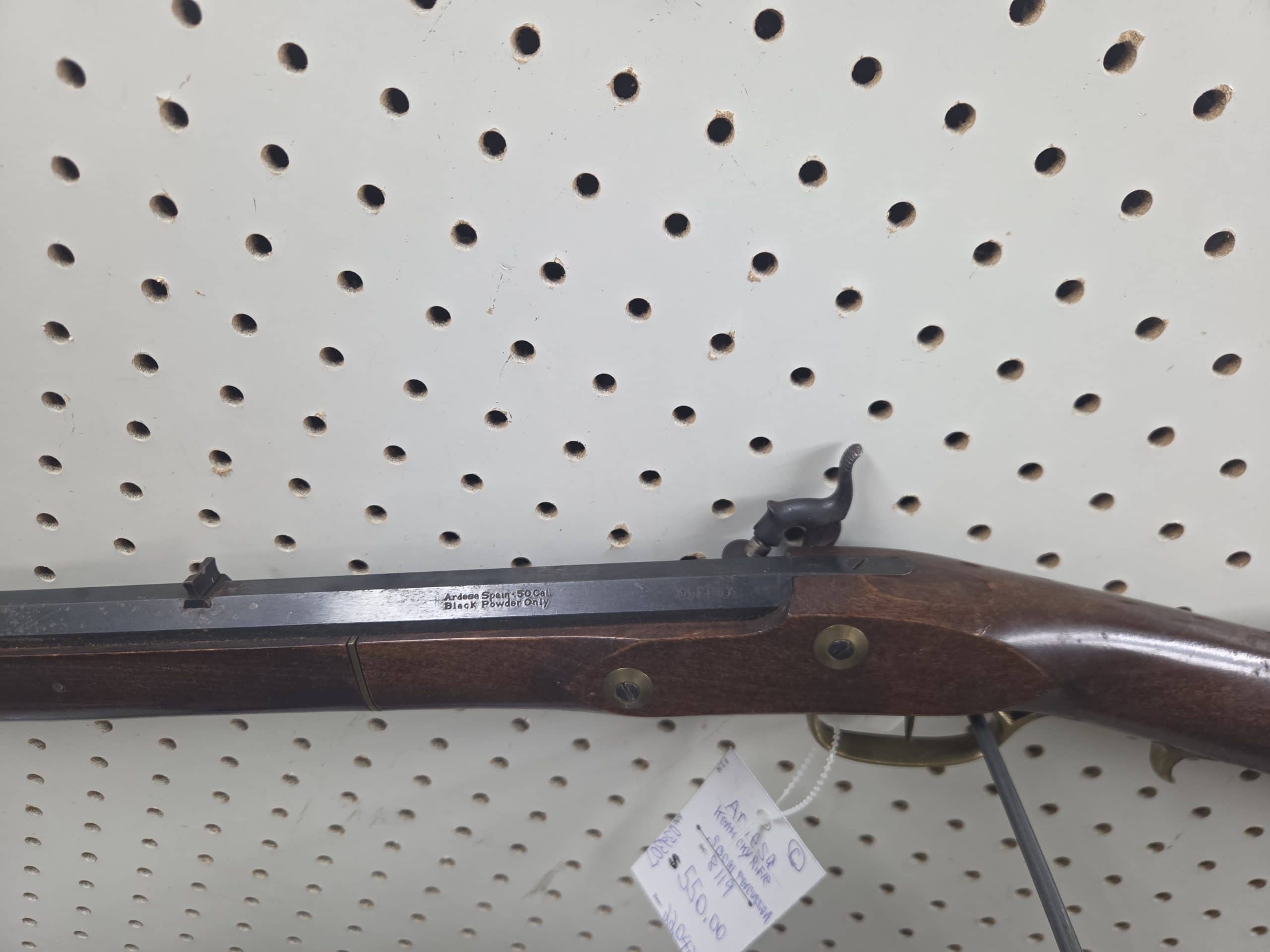 Ardesa 2 A side view of a 20261018_092811 (1) black powder rifle with a wooden stock, hanging on a pegboard with a price tag attached.