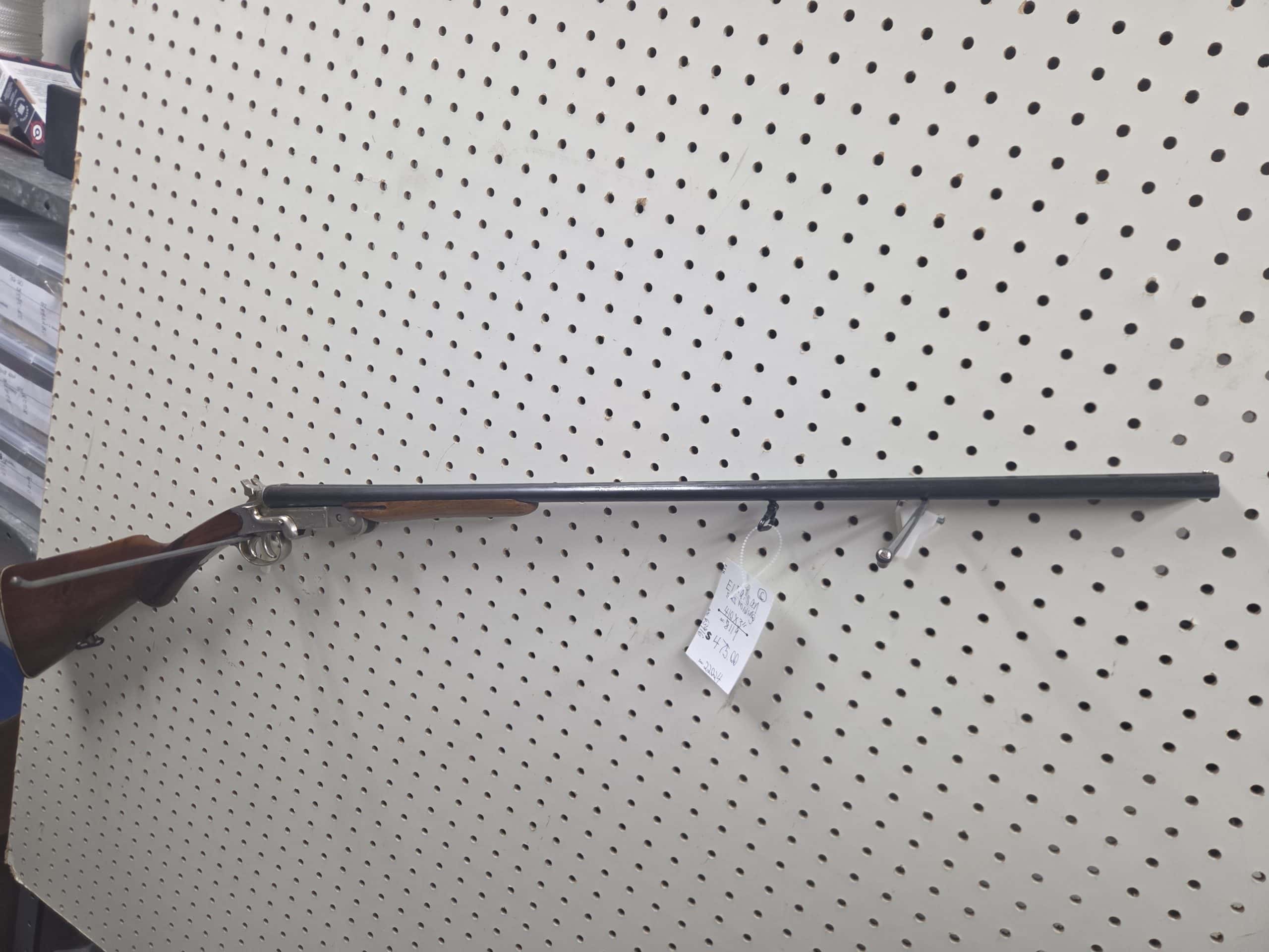El Faisan 2 A 20261018_092948 side-by-side double-barrel shotgun with a wooden stock hanging on a pegboard wall with a price tag attached.