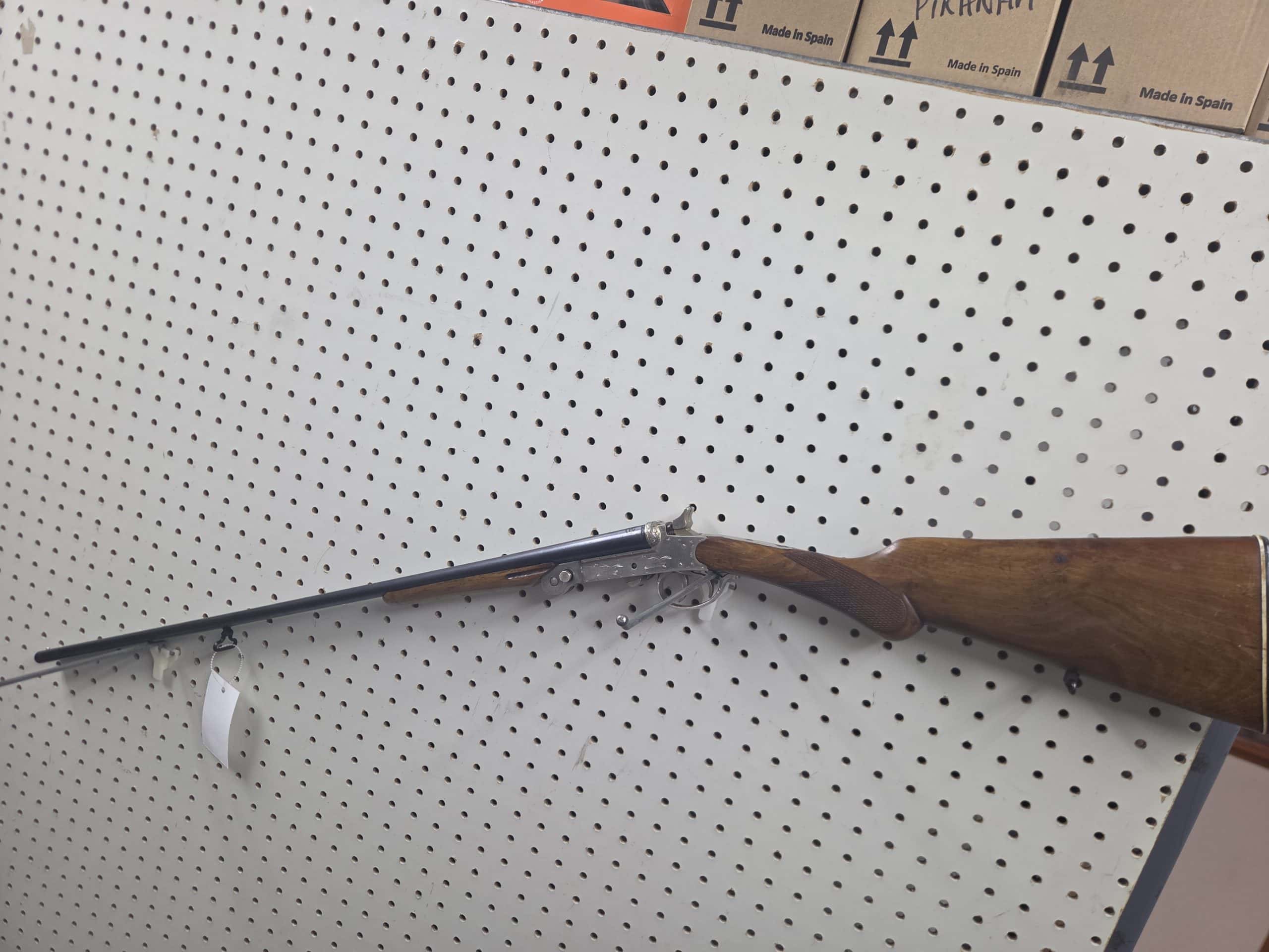 El Faisan 3 A break-action single-shot shotgun 20261018_092959 with a wooden stock mounted on a pegboard wall.