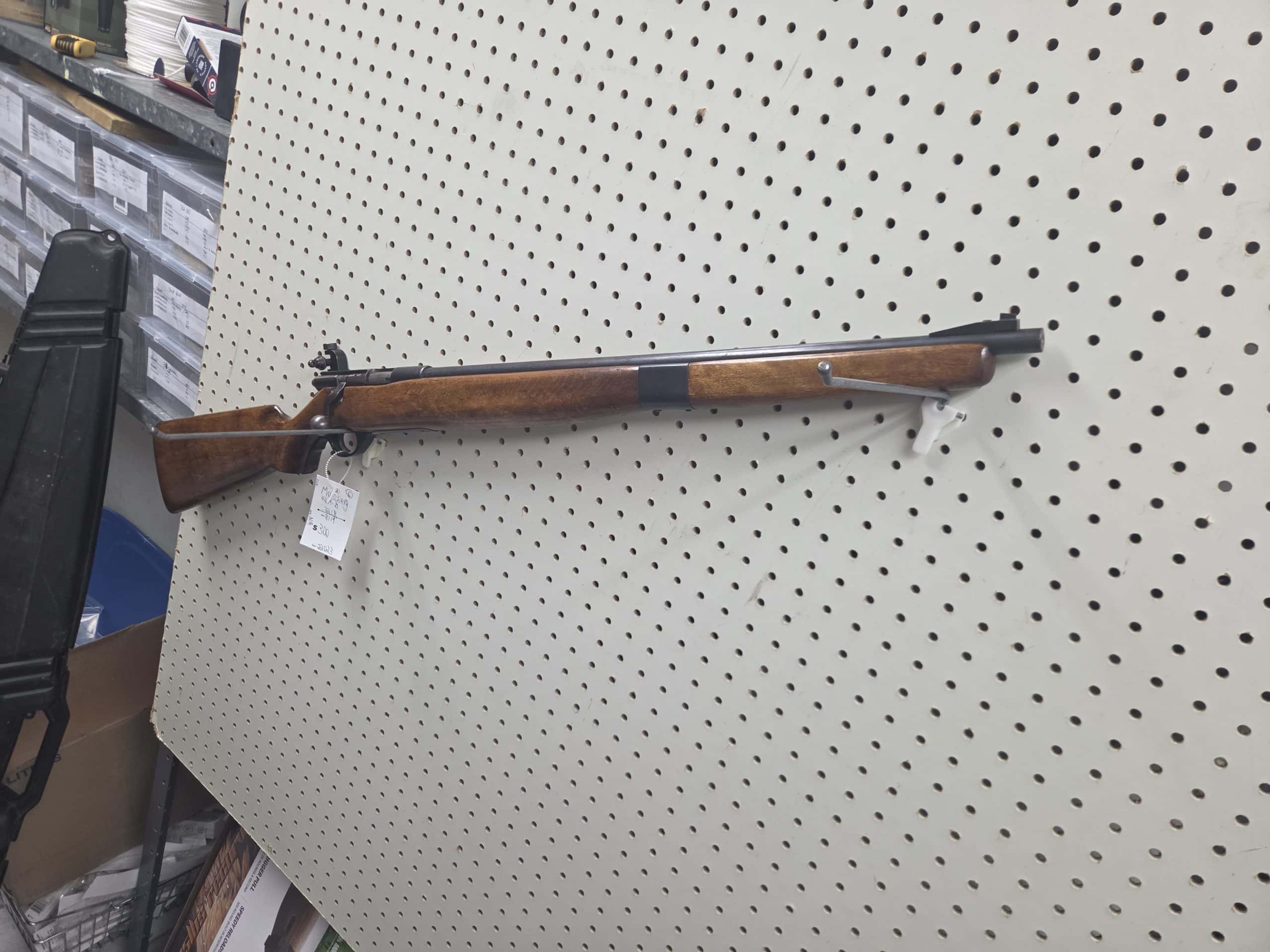 Mossberg 2 20261018_093147 bolt-action rifle with a wood stock hanging on a pegboard wall.