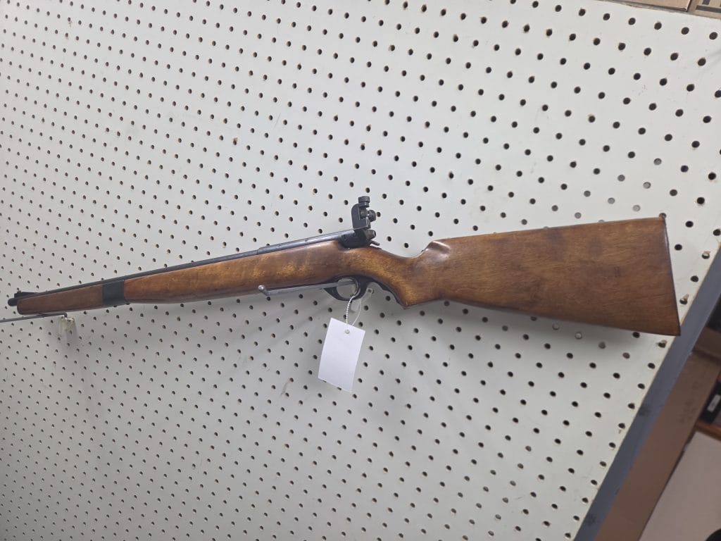 20261018_093158 bolt-action rifle with a wooden stock mounted on a white pegboard wall.
