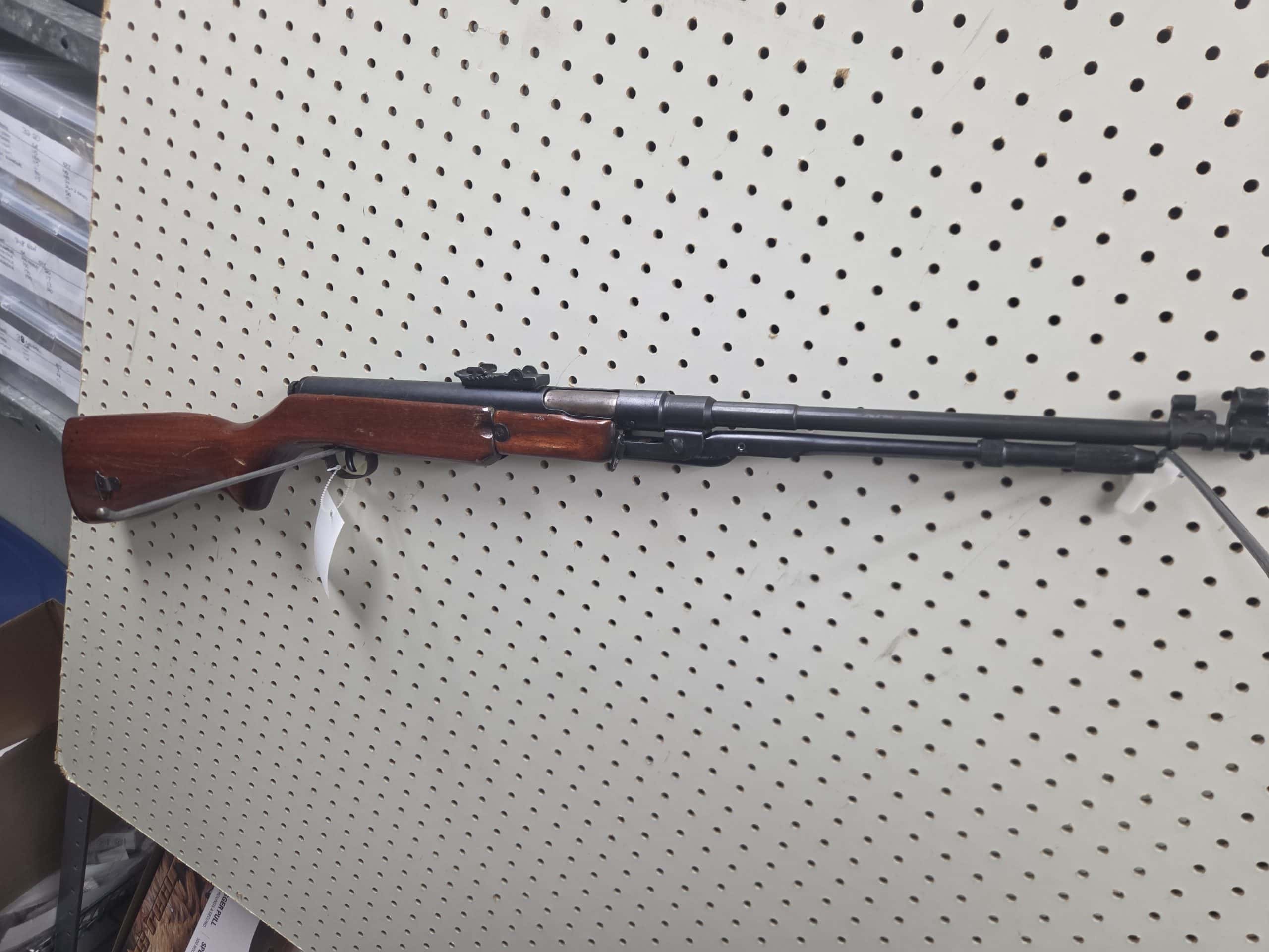 Arrow 2 20261018_093950 bolt-action rifle with a wooden stock mounted on a pegboard wall.