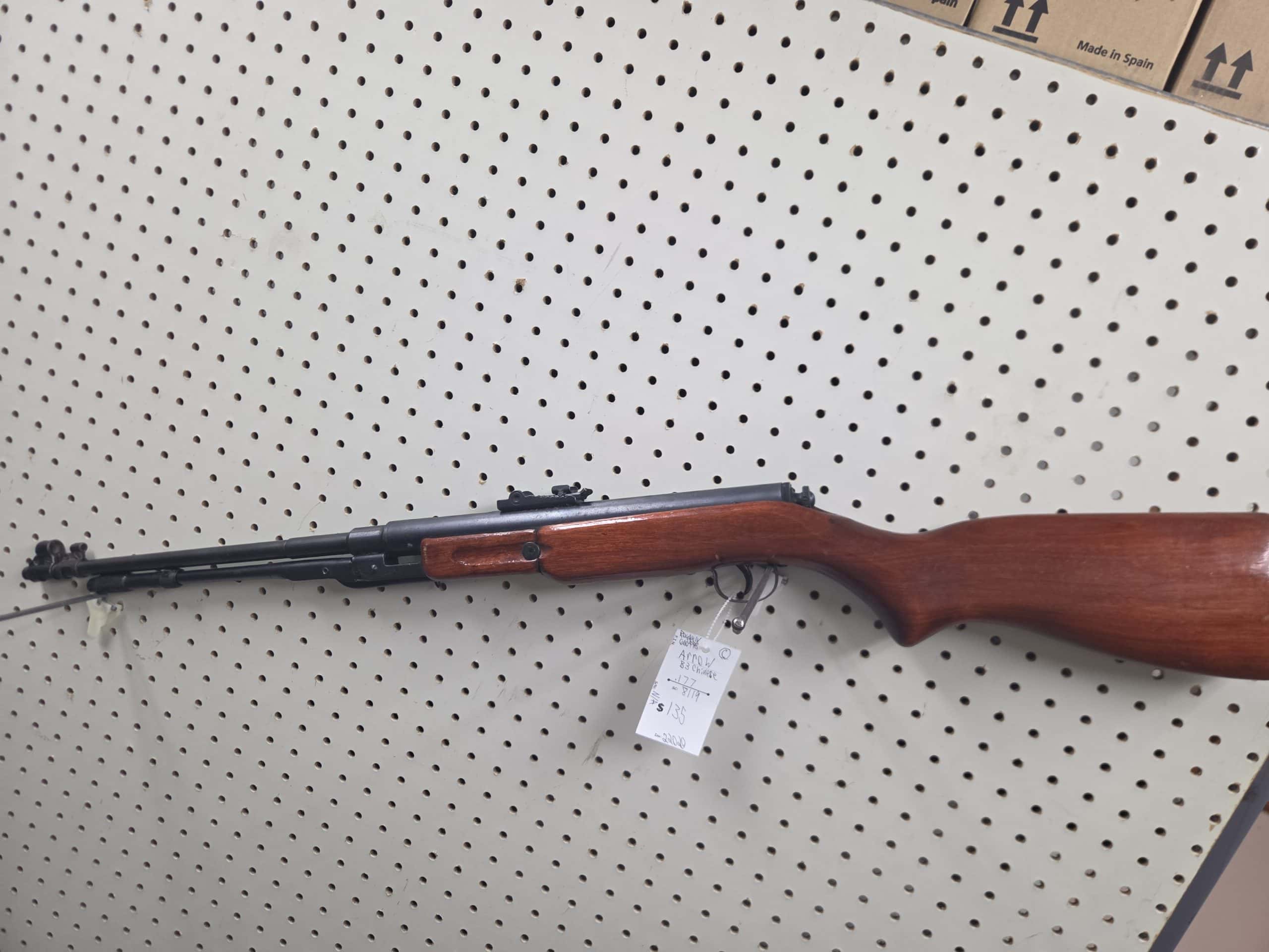 Arrow 1 A 20261018_094001 air rifle with a wooden stock hanging on a white pegboard, featuring a price tag attached to the trigger guard.