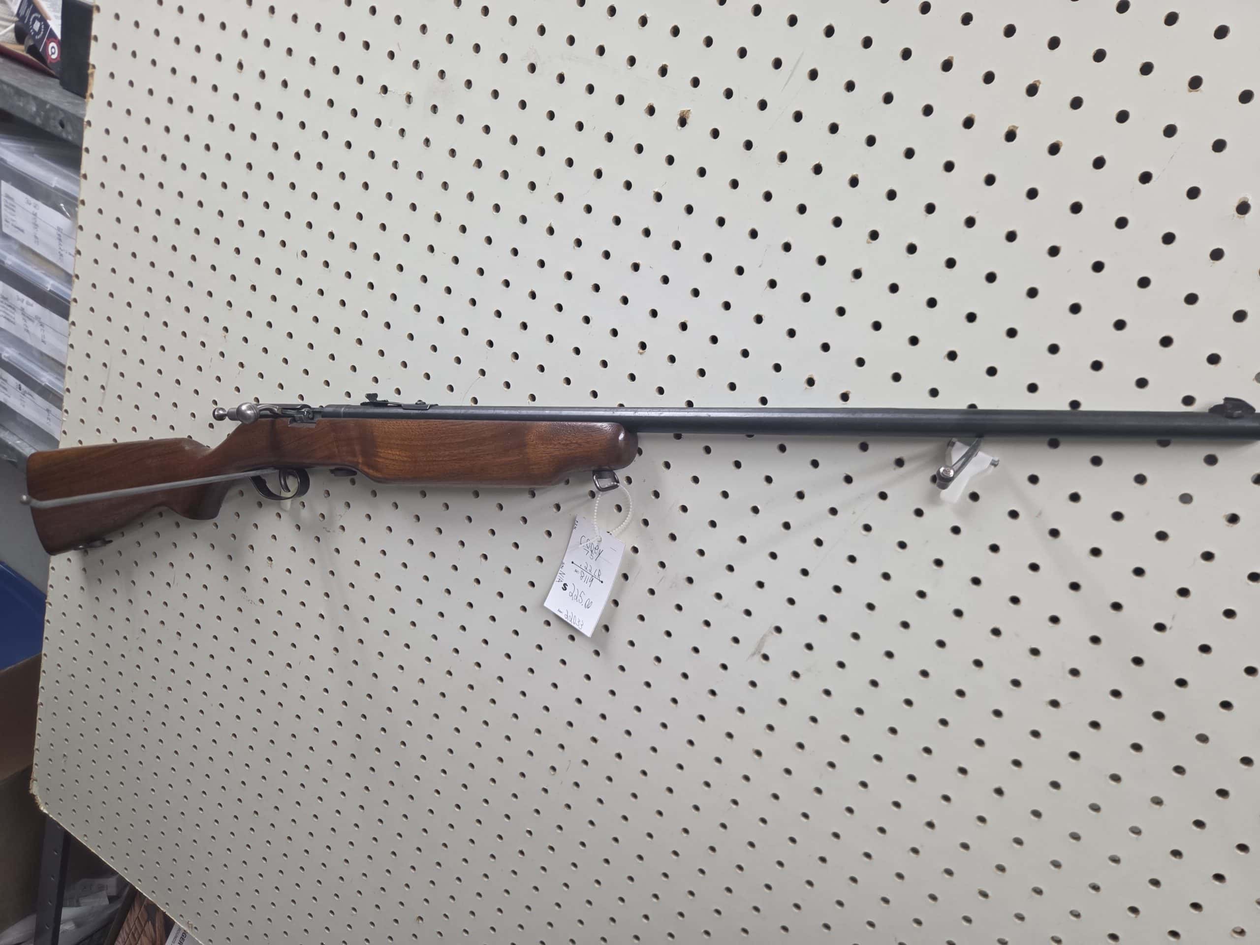 Cooey 1 20261018_094108 bolt-action rifle with a wood stock hanging on a white pegboard, with a price tag attached.
